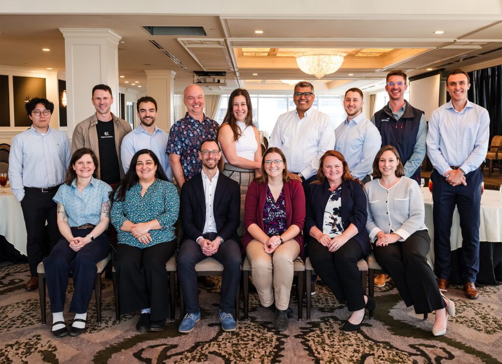 Group of professionals posing for a group photo in a conference room, with people standing in back and seated in front, all smiling.